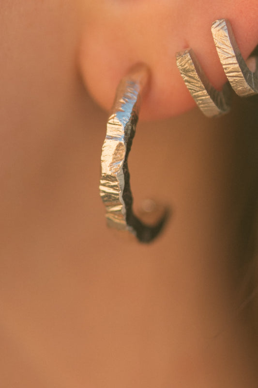 Close-up of an ear wearing a wide gold vermeil hoop with a rough, hand-hammered edge