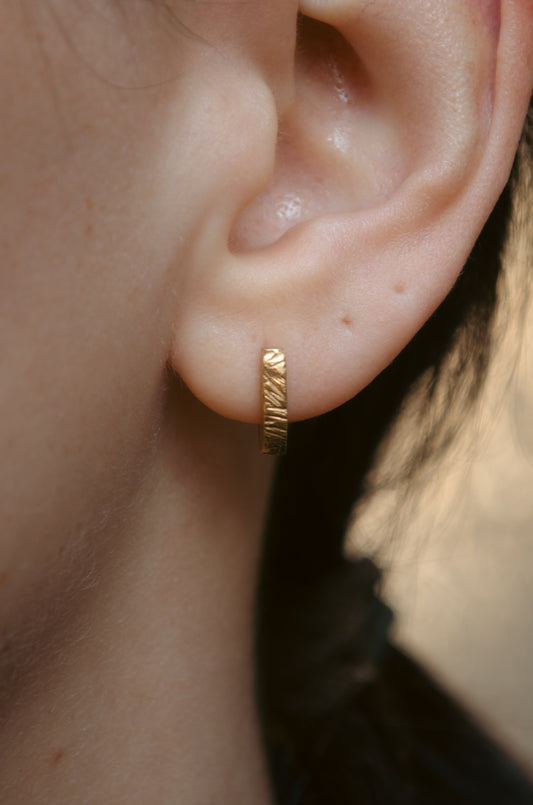 Close-up of an ear wearing a small textured gold vermeil huggie hoop
